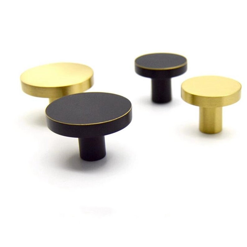 May include: Four round cabinet knobs, two are gold and two are black. The knobs have a flat top and a short, round stem.
