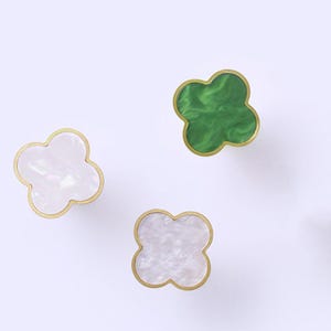 May include: Three decorative brass knobs with a four-leaf clover design. The knobs have a green, white, and iridescent finish.