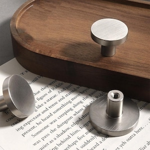 May include: Three silver round cabinet knobs with a brushed finish. The knobs have a round base and a cylindrical stem.