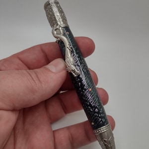 May include: A silver pen with a dragon design on the top and a black and green snakeskin pattern on the barrel.