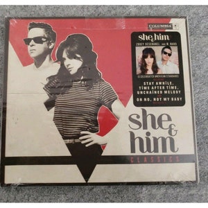 May include: A CD cover featuring a black and white photo of a man and woman. The album title is "she & him" and the text "Classics" is below the title. The album cover is red and white with a black and white photo of the band members.