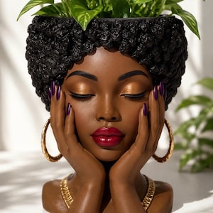 Peut inclure: Un cache-pot décoratif en forme de tête représentant un visage à la peau foncée, yeux fermés, fard à paupières doré et lèvres rouges. Il présente des cheveux noirs texturés, des créoles dorées, un collier chaîne et des ongles violets.