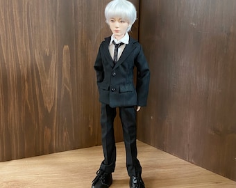 May include: A doll wearing a black suit with a white shirt and a black tie. The doll has white hair and is standing on a wooden surface.
