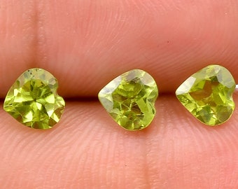 May include: Three heart-shaped peridot gemstones in various shades of green. The gemstones are faceted and have a polished finish.