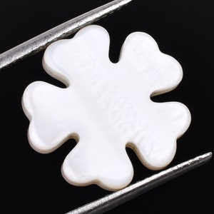 Könnte beinhalten: Weißer Perlmutt-Blumenanhänger mit fünf Blütenblättern. Der Anhänger wird von einer Pinzette gehalten.