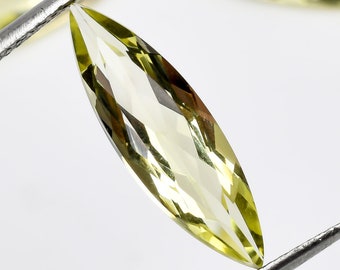 May include: A marquise cut, light yellow gemstone held by tweezers. The gemstone is faceted and has a high level of clarity.