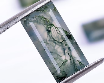 May include: A green moss agate gemstone with a rectangular shape and a clear, translucent appearance. The stone has a unique pattern of green moss-like inclusions.