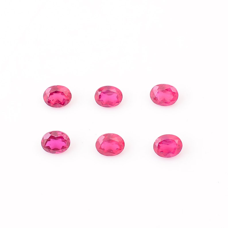 Puede incluir: Seis piedras preciosas ovaladas de color rosa brillante sobre un fondo blanco.