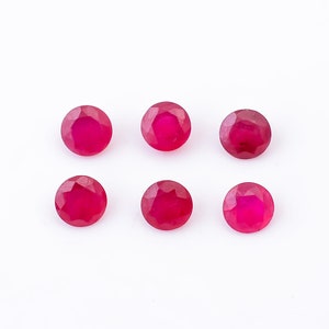 May include: Six round, faceted ruby gemstones, each with a deep red color, arranged in two rows of three on a white background.