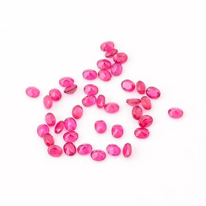 Puede incluir: Una dispersi&oacute;n de piedras preciosas rosadas facetadas de forma ovalada sobre un fondo blanco.