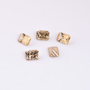 May include: Five faceted, rectangular, light brown gemstones on a white background.