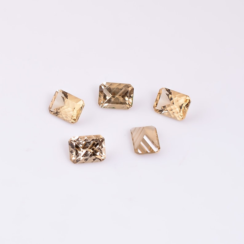 May include: Five faceted, rectangular, light brown gemstones on a white background.