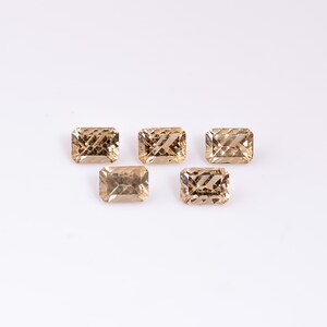 May include: Five light brown, faceted, rectangular gemstones on a white background.