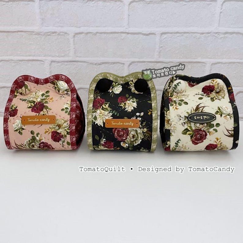 May include: Three floral fabric pouches in pink, black, and cream, each with a unique design. The pouches feature a repeating floral pattern with red and white roses. Each pouch has a small, rectangular tag that reads "Tomato candy".