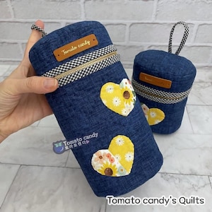 May include: Two blue denim fabric zippered pouches with a black and white checkered trim. The pouches are decorated with yellow and white floral heart-shaped patches. The larger pouch has the text "Tomato candy" on a brown label. The smaller pouch has the text "Tomato candy" on a brown label. The text "Tomato candy's Quilts" is at the bottom of the image.