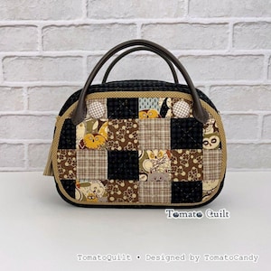 Op de afbeelding: Een gewatteerde handtas met een patchworkontwerp van zwarte, bruine en beige vierkanten met uilen- en bloemenpatronen. De tas heeft twee donkerbruine handvatten, een beige rand en twee ronde stoffen accenten. Tekst leest TomatoQuilt TomatoCandy.
