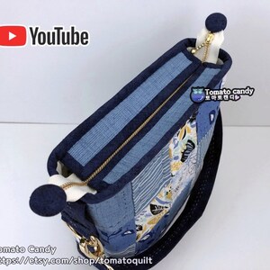 Pode incluir: Uma bolsa tote de tecido patchwork azul e branco com um z&iacute;per dourado e uma al&ccedil;a azul marinho. A bolsa tem um pequeno remendo redondo azul marinho com o texto "Tomato candy" em branco e um cora&ccedil;&atilde;o rosa.