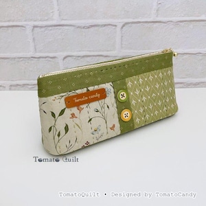 May include: A rectangular pencil case with a floral pattern and green accents. The case features a zipper closure, two decorative buttons, and a leather tag that reads "Tomato candy". The text "TomatoQuilt" and "Designed by TomatoCandy" are also visible.