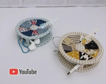 May include: Two round, fabric-covered cable organizers with zippered closures. The left organizer features blue and floral patchwork with a light blue gingham border. The right organizer features brown, yellow, and black patchwork with a beige gingham border.