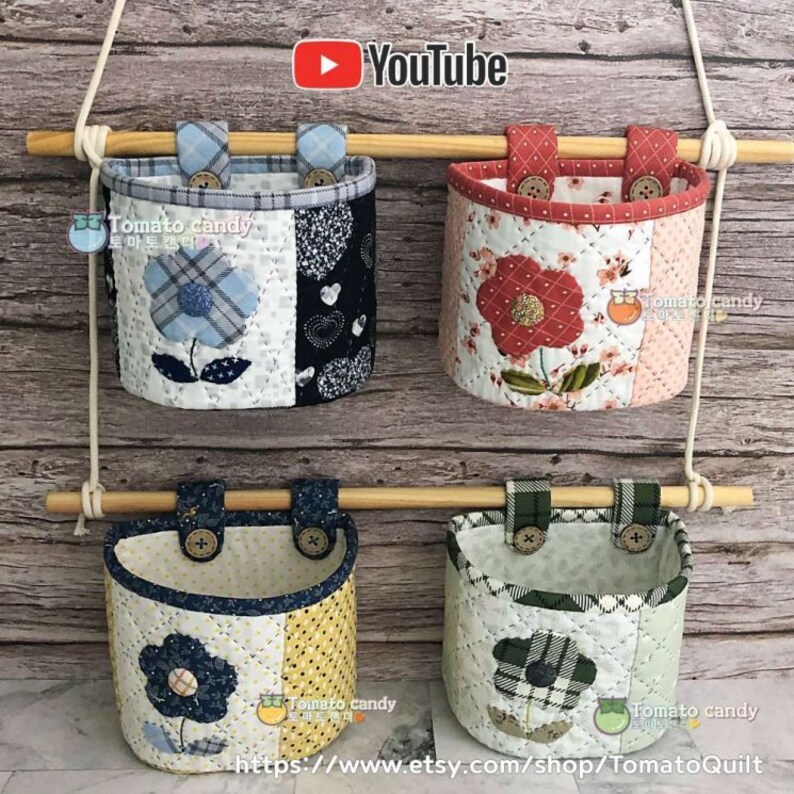 May include: Four fabric wall pockets with floral designs hang from a wooden dowel rod. The pockets are made of quilted fabric with different patterns and colors, including blue, red, yellow, and green. The pockets are labeled with the text "Tomato candy" and a YouTube logo is visible in the top center of the image.