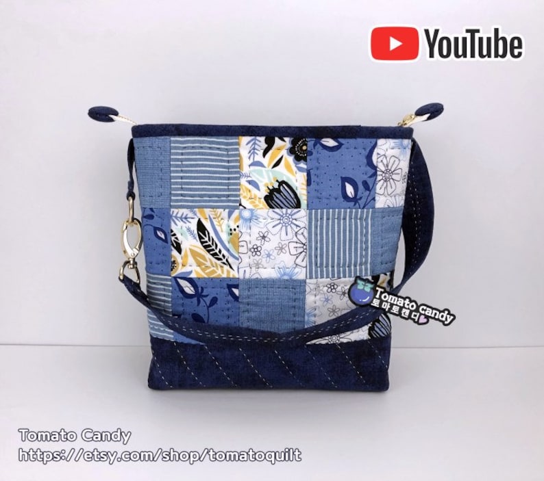Pode incluir: Uma bolsa tote de tecido patchwork azul e branco com uma al&ccedil;a longa. A bolsa tem um fecho de correr e uma pequena etiqueta de tecido azul e branco que diz "Tomato candy".
