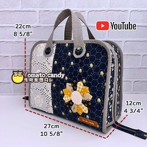 May include: A blue and white quilted fabric cosmetic bag with a yellow flower design. The bag has a zipper closure and a top handle. It measures 8 5/8 inches tall, 10 5/8 inches wide, and 4 3/4 inches deep.