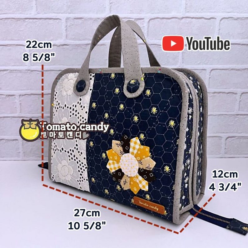 May include: A blue and white quilted fabric cosmetic bag with a yellow flower design. The bag has a zipper closure and a top handle. It measures 8 5/8 inches tall, 10 5/8 inches wide, and 4 3/4 inches deep.