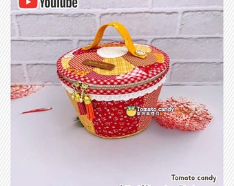 May include: A round, quilted fabric storage container featuring a patchwork design in shades of red, yellow, and white. It includes a yellow handle, a zippered lid with two tassels, and a brown label with the text Tomato candy.