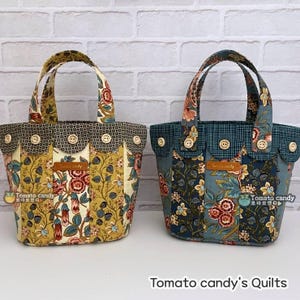 May include: Two fabric tote bags with floral patterns and scalloped tops featuring wooden buttons. The left bag is yellow and the right bag is blue. Both have a brown leather label reading Tomato candy. The text Tomato candy Quilts is below.
