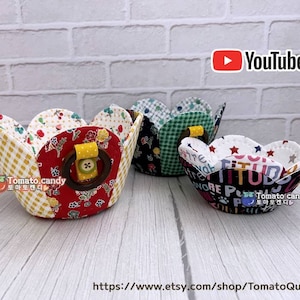 Peut inclure: Trois paniers en tissu avec des motifs diff&eacute;rents. Les paniers sont en forme de p&eacute;tales de fleurs et ont une poign&eacute;e en bois. Les paniers sont sur une surface en bois blanc. Le texte "Tomato candy" est visible sur les paniers.