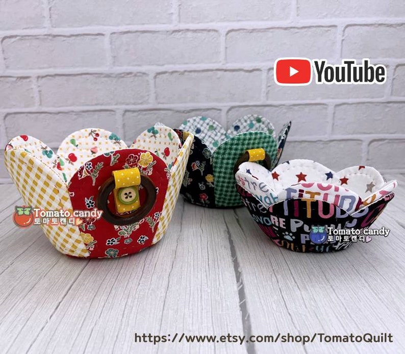 Peut inclure: Trois paniers en tissu avec des motifs diff&eacute;rents. Les paniers sont en forme de p&eacute;tales de fleurs et ont une poign&eacute;e en bois. Les paniers sont sur une surface en bois blanc. Le texte "Tomato candy" est visible sur les paniers.