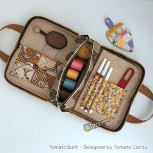 May include: An open brown zippered pouch with a handle, filled with sewing supplies. The pouch has a brown and yellow floral pattern and contains spools of thread, a small sewing kit, a pair of scissors, and a few pens.