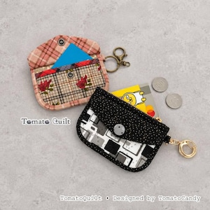 May include: Two fabric coin pouches with key rings. One features a pink plaid pattern with red floral accents and a blue card insert. The other is black with white polka dots, a geometric pattern, and a yellow card insert. Two silver coins are nearby.