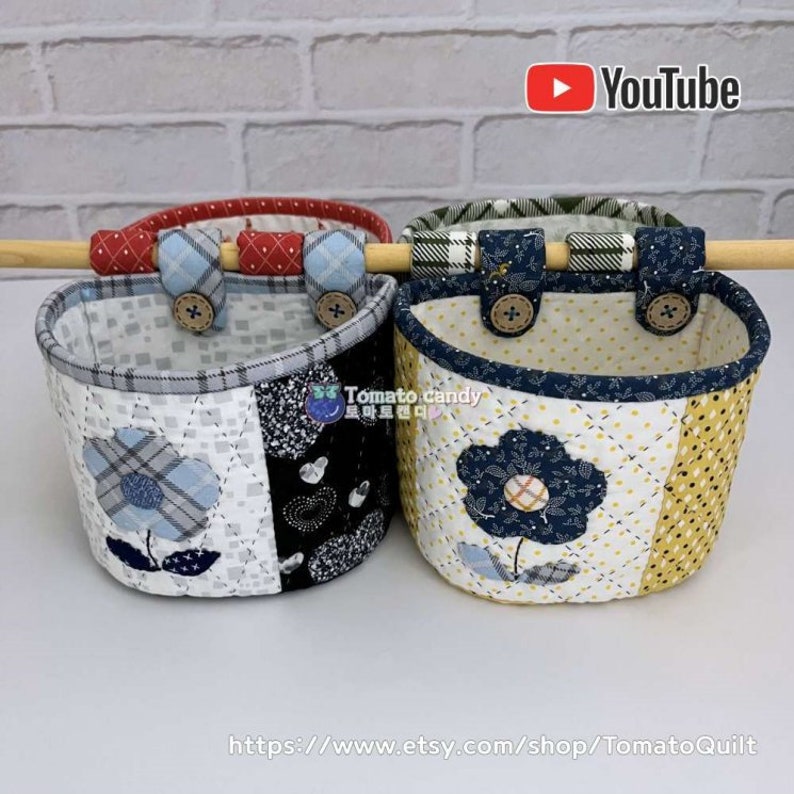 May include: Three quilted fabric hanging baskets with different patterns and colors. The baskets are made of patchwork fabric with floral designs and plaid patterns. The baskets are hanging from a wooden dowel rod. The baskets are labeled with the text "Tomato candy".