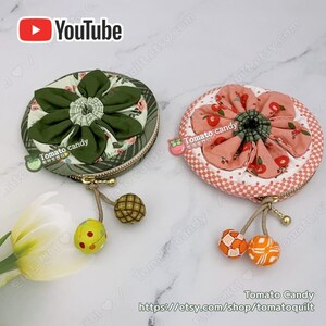 K&ouml;nnte beinhalten: Zwei runde M&uuml;nzbeutel mit floralen Stoffdesigns. Der Beutel links hat ein gr&uuml;nes Blumenmuster mit einem gr&uuml;nen Rei&szlig;verschluss. Der Beutel rechts hat ein rosafarbenes Blumenmuster mit einem goldenen Rei&szlig;verschluss. Beide Beutel haben einen kleinen Quasten mit einer Stoffkugel am Ende.