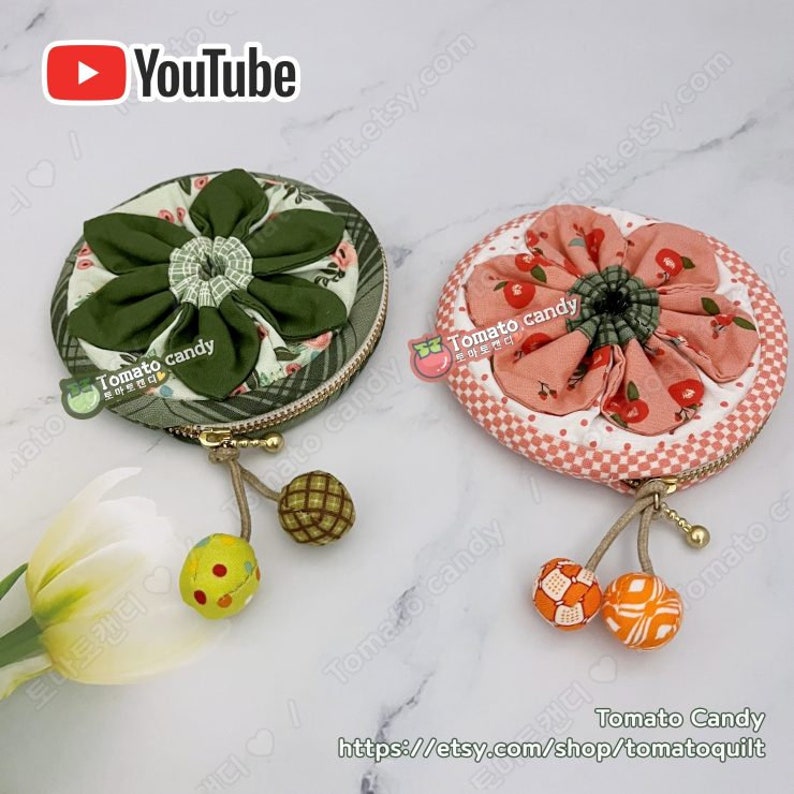 K&ouml;nnte beinhalten: Zwei runde M&uuml;nzbeutel mit floralen Stoffdesigns. Der Beutel links hat ein gr&uuml;nes Blumenmuster mit einem gr&uuml;nen Rei&szlig;verschluss. Der Beutel rechts hat ein rosafarbenes Blumenmuster mit einem goldenen Rei&szlig;verschluss. Beide Beutel haben einen kleinen Quasten mit einer Stoffkugel am Ende.