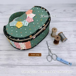 May include: A semi-circular quilted storage case in sage green with a floral pattern, featuring a zipper closure, a handle, and a colorful patchwork accent. Includes two wooden thread spools, metal embroidery scissors, and a brown label reading Tomato candy.
