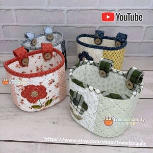 May include: Four quilted fabric storage baskets with handles and buttons. The baskets are in various colors and patterns, including red, green, blue, and yellow. The baskets are all in the same style and have a rounded shape. The baskets are perfect for organizing small items in a home or office.