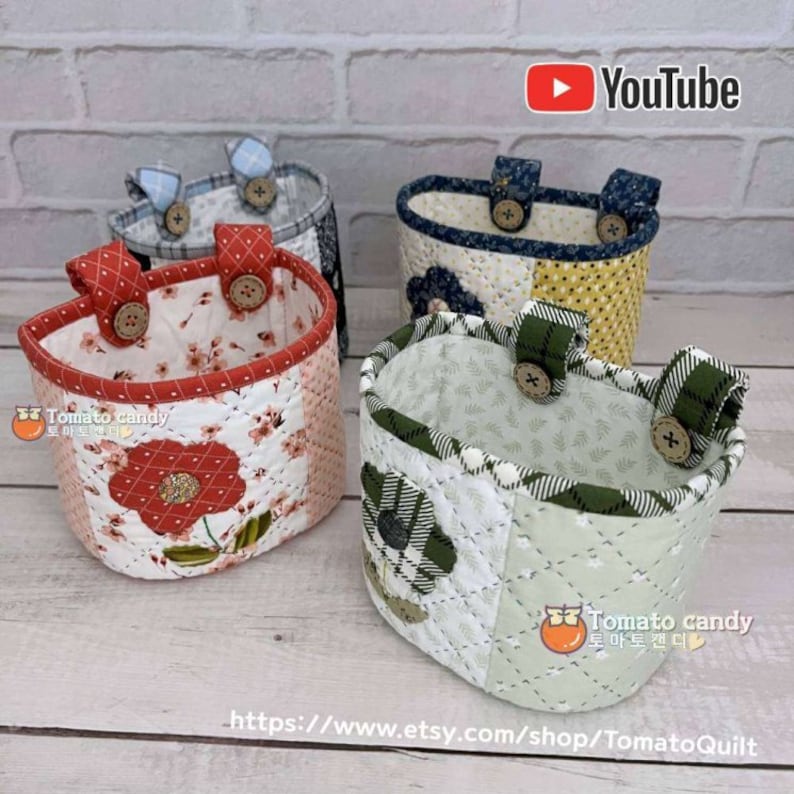 May include: Four quilted fabric storage baskets with handles and buttons. The baskets are in various colors and patterns, including red, green, blue, and yellow. The baskets are all in the same style and have a rounded shape. The baskets are perfect for organizing small items in a home or office.