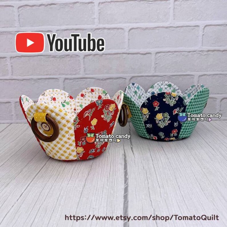 Peut inclure: Deux paniers en tissu avec des bords festonn&eacute;s et des poign&eacute;es en bois. Les paniers sont faits de tissu patchwork avec des motifs floraux en rouge, jaune, bleu et vert. Les paniers sont pos&eacute;s sur une surface en bois blanc. Le texte "Tomato candy" est visible sur les paniers.