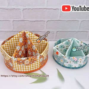 Pode incluir: Duas cestas de armazenamento de tecido com forma circular e compartimentos divididos. A cesta à esquerda é amarela e laranja com um padrão floral e um padrão xadrez. A cesta à direita é azul-turquesa e branca com um padrão floral. Ambas as cestas têm um fecho de botão e um rótulo que diz "Tomato Candy".