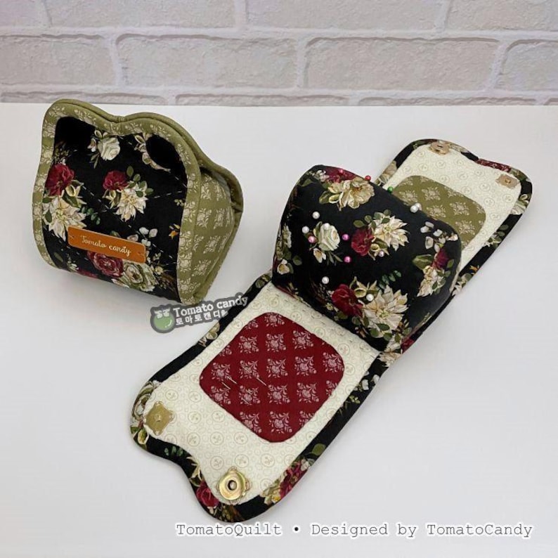 May include: Two handmade fabric items. One is a small, floral-patterned pouch with a label that reads "Tomato candy". The other is a larger, foldable item with a floral pattern, a red patterned center, and a magnetic closure. The items are designed by TomatoCandy.