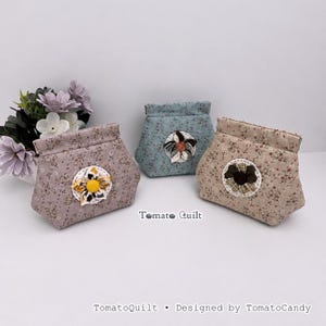 May include: Three fabric pouches with floral patterns in mauve, blue, and beige. Each pouch features a central fabric flower embellishment and a top flap closure. The text TomatoQuilt and TomatoQuilt • Designed by TomatoCandy are visible.