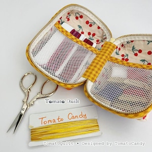 May include: An open yellow gingham fabric case with a cherry print lining and mesh pockets, accompanied by silver embroidery scissors and a card labeled Tomato Candy with yellow embroidery floss wrapped around it.
