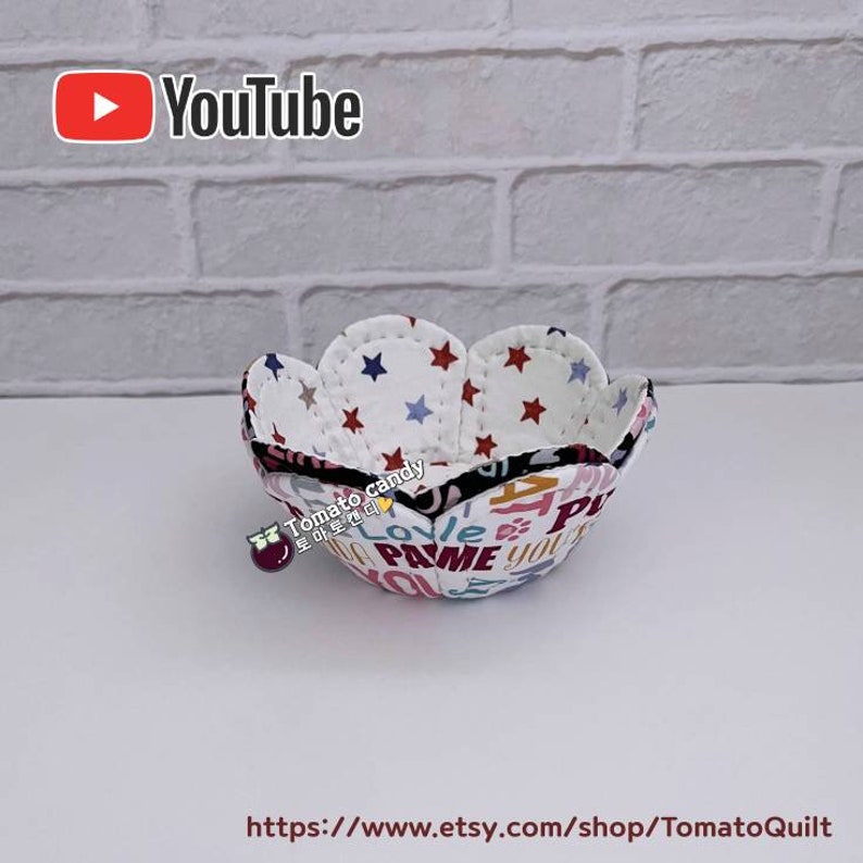Peut inclure: Un bol en tissu blanc avec un bord festonn&eacute; et un imprim&eacute; color&eacute; de mots et d'&eacute;toiles. Le bol est fait de tissu et est parfait pour contenir de petits objets.