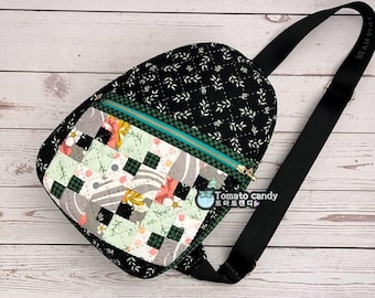 Puede incluir: Una mochila bandolera acolchada de tela negra con estampado de hojas blancas y un bolsillo frontal con diseño de patchwork de cuadrados verdes, blancos y florales. Tiene una cremallera dorada, una correa negra ajustable y el texto Tomato Candy.