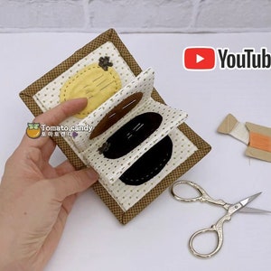 May include: A brown and white fabric pincushion with a yellow, brown, and black fabric design. The pincushion is folded closed and has a YouTube logo in the background.