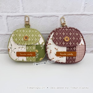 May include: Two small, round fabric pouches with gold-colored keychains. One is green with floral and geometric patterns, the other is burgundy with white floral accents. Each has a wooden button and a leather tag that reads "Tomato candy."