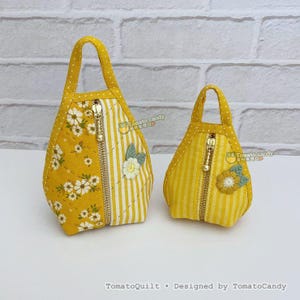 Peut inclure: Deux petits sacs en tissu jaune avec des poignées et des fermetures éclair. L'un des sacs présente un motif floral, l'autre des rayures verticales. Les deux sacs ont une application de fleur et le texte "Tomato candy" et "TomatoQuilt • Designed by TomatoCandy".