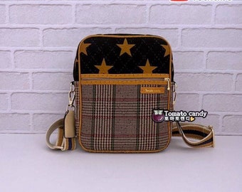 May include: A rectangular crossbody bag featuring a black quilted upper section with gold stars and a lower section in a brown, beige, and red plaid pattern. It includes a zippered front pocket, gold hardware, and an adjustable striped shoulder strap.